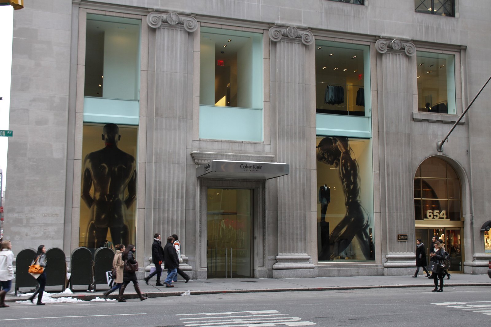 The grey stone facade of the Calvin Klein Collection store at 654 Madison Avenue in New York, with tall display windows and pedestrians on the sidewalk.
