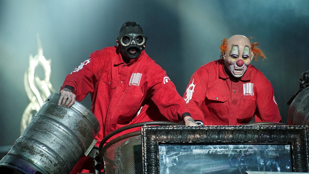 Two masked Slipknot members in red jumpsuits performing on stage behind percussion.