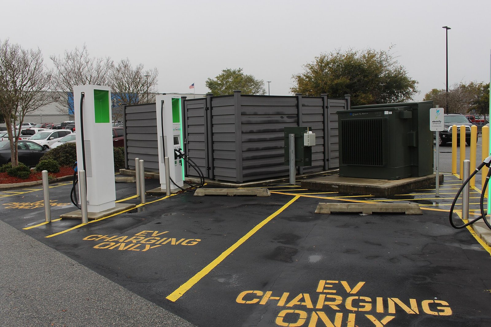 Electric vehicle fast chargers in a parking lot with yellow 'EV charging only' markings painted on the pavement.