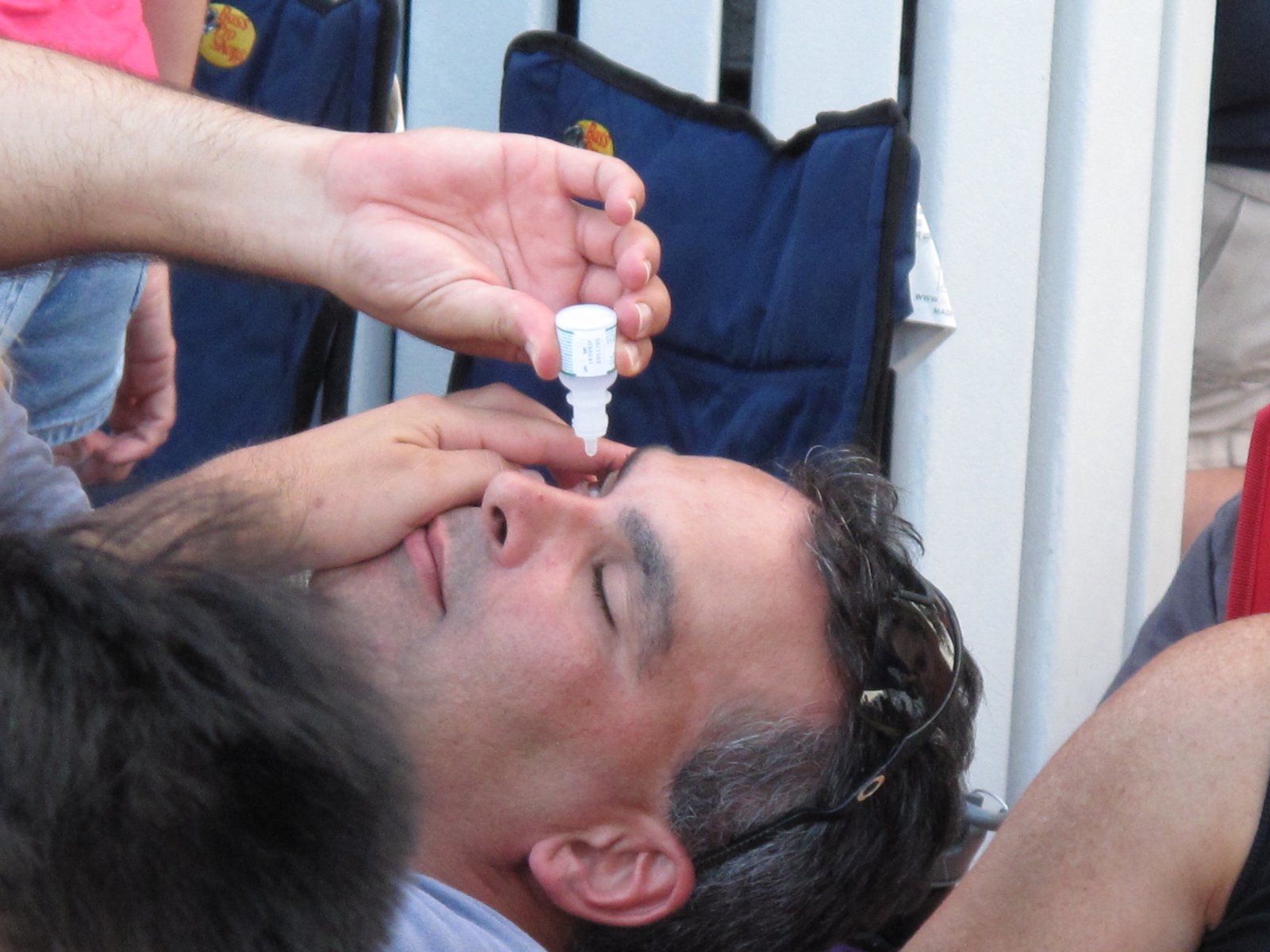 A man tilting his head back and squeezing a drop from a small plastic bottle into his eye.