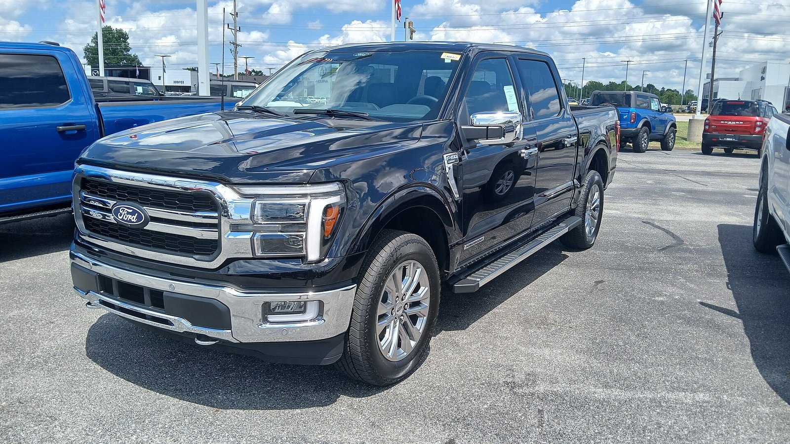 A black 2024 Ford F-150 Lariat crew cab pickup truck parked on a dealership lot, seen from the front left.