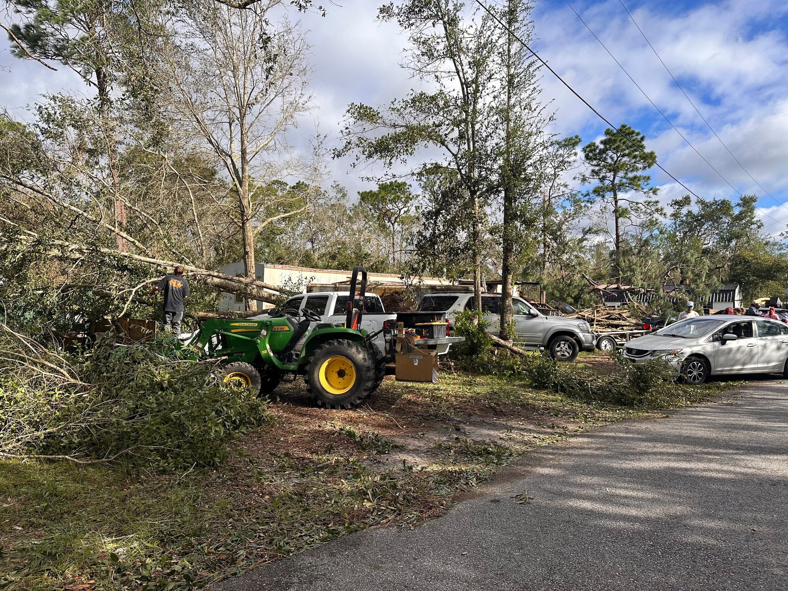 Storm damage in East Milton, Florida, after Hurricane Isaias, with broken trees and debris around buildings under a grey sky.