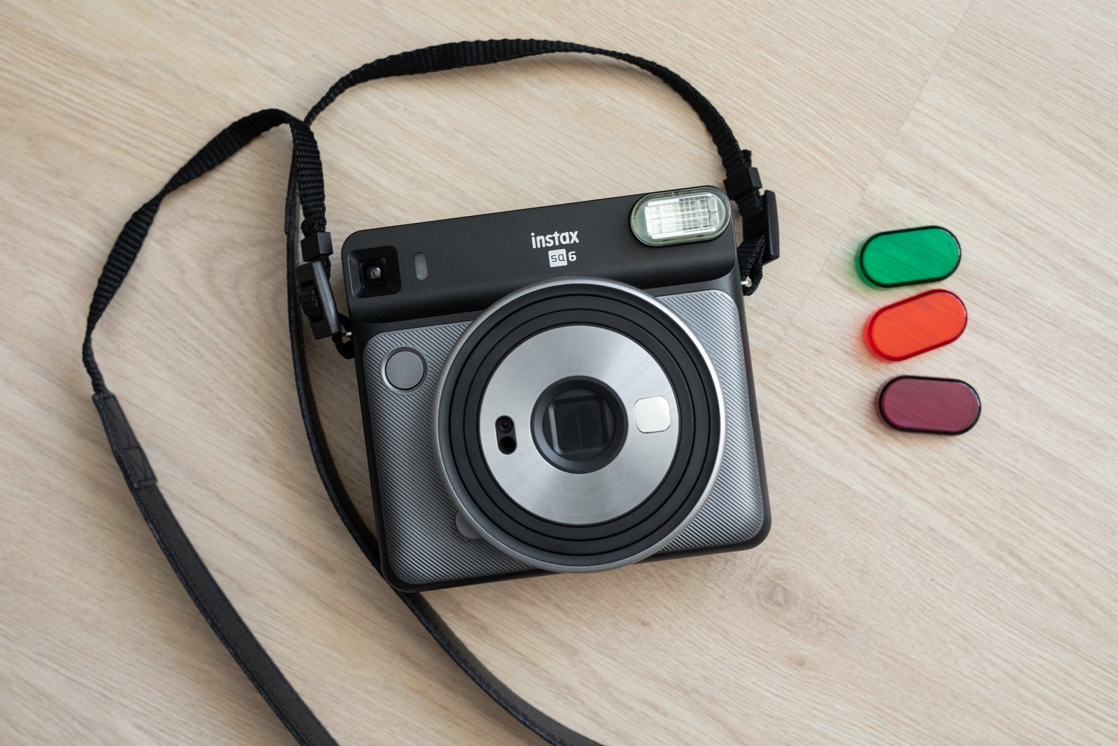 A Fujifilm Instax SQ6 square-format instant camera with a round lens barrel and flash, photographed on a plain background.