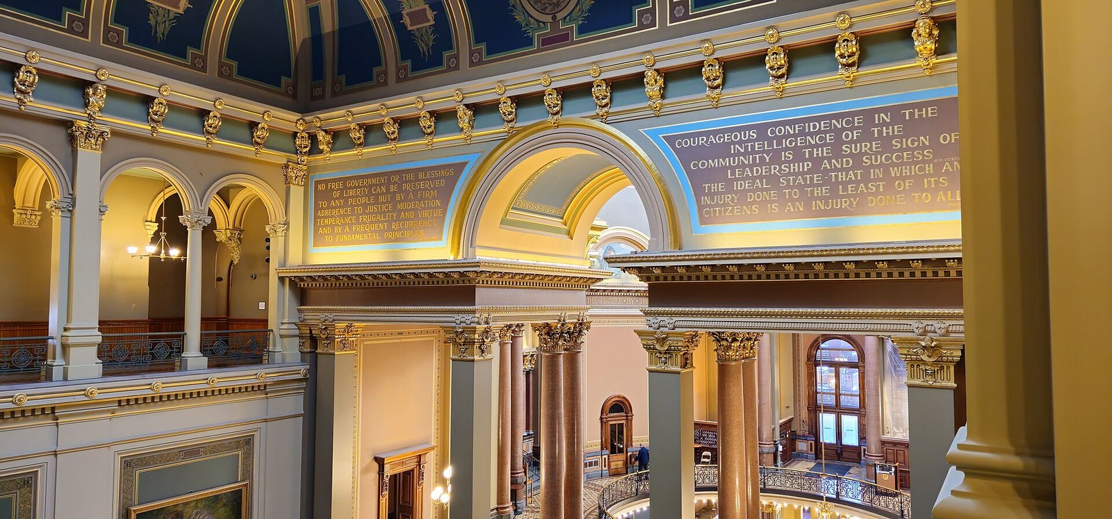 Ornate interior of the Iowa State Capitol, with gilded columns, painted arches and balconied galleries beneath a decorated ceiling.