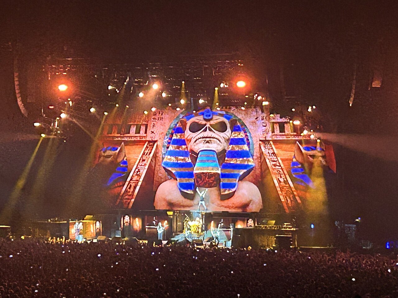 Iron Maiden's Egyptian-themed stage set glows orange and gold above a packed arena floor during the song Powerslave.