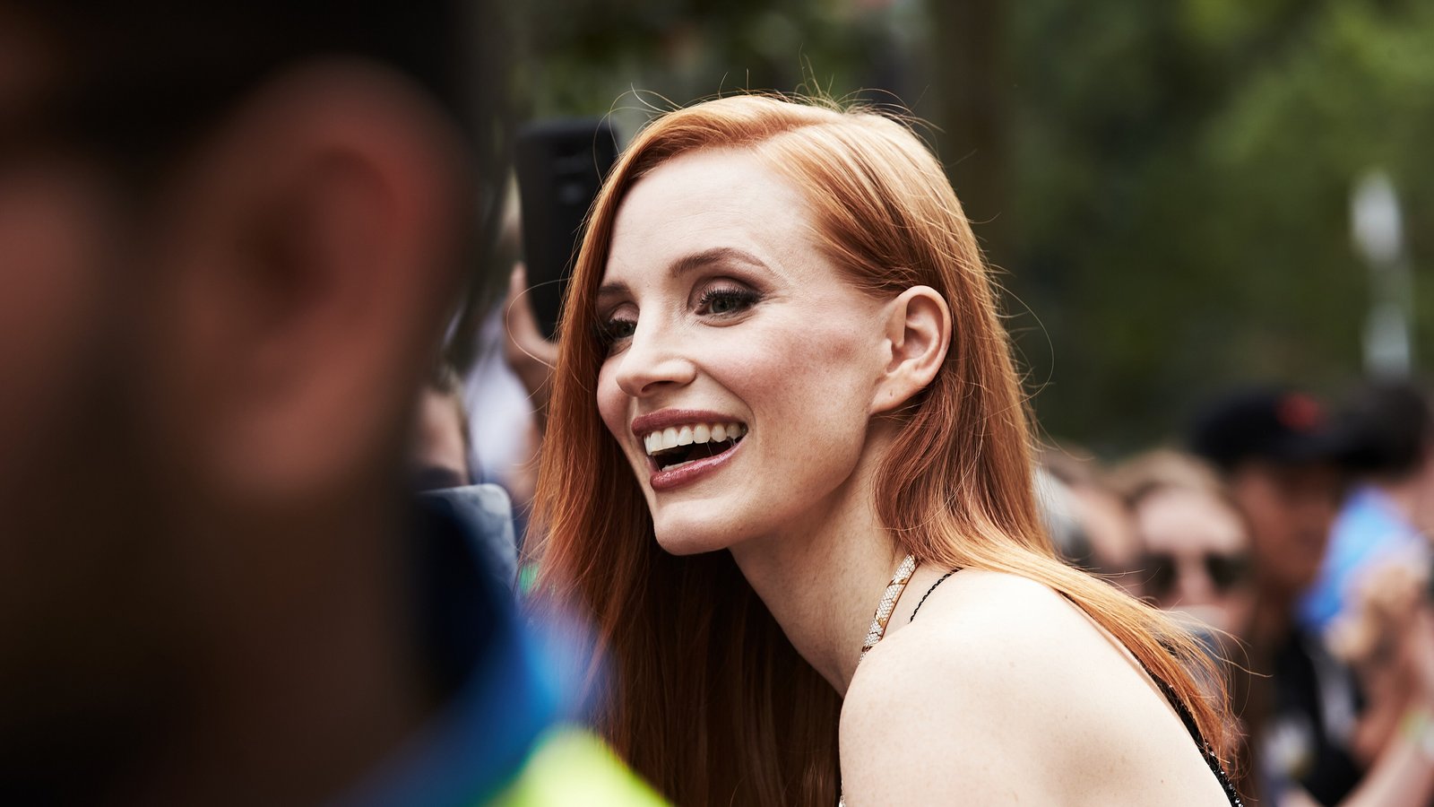 Jessica Chastain, with long red hair, smiles broadly as she greets fans at the Toronto International Film Festival.