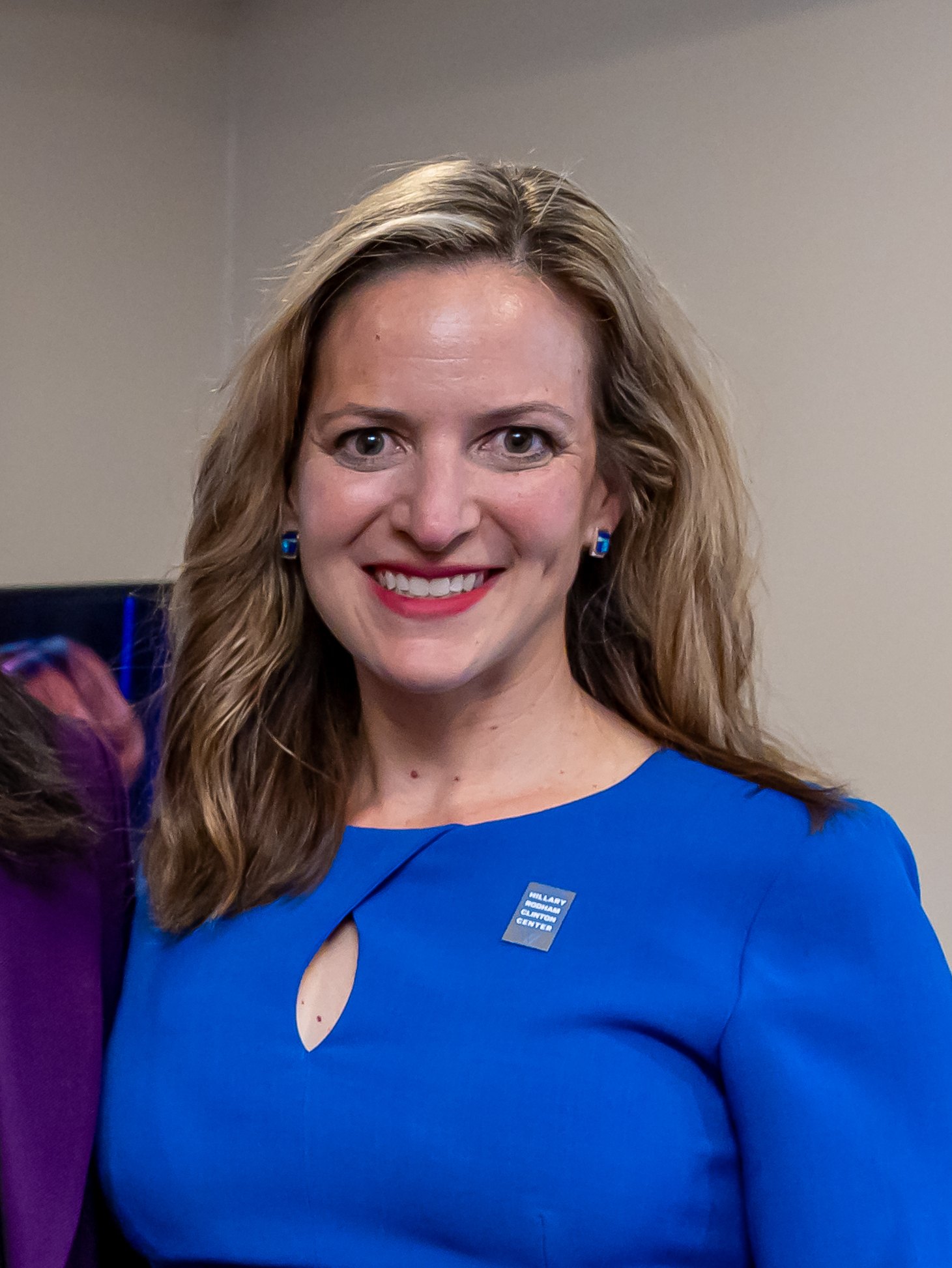 Michigan Secretary of State Jocelyn Benson, with long hair and a blue dress, smiles at an event.
