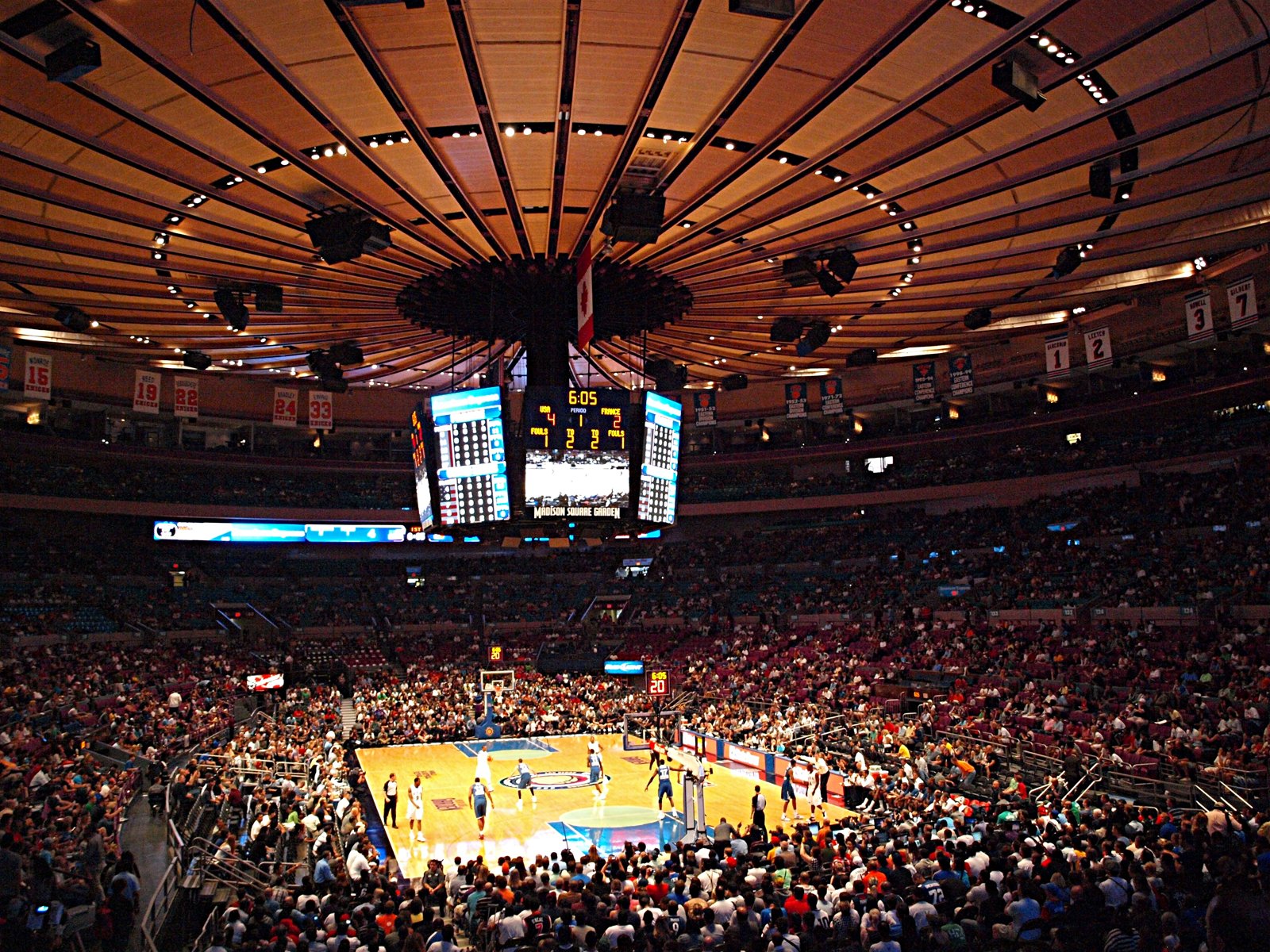 Packed crowd inside Madison Square Garden looking down at the basketball court beneath the arena's circular ceiling and center-hung scoreboard.