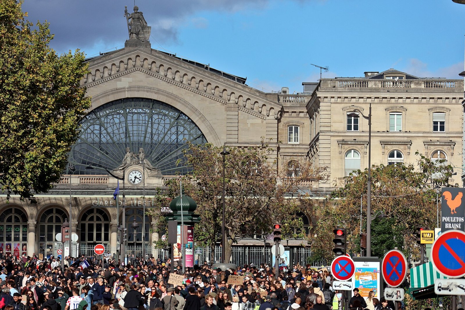 A large crowd of demonstrators filling the street in front of the Gare du Nord railway station in Paris, with its glass arches and stone statues above.