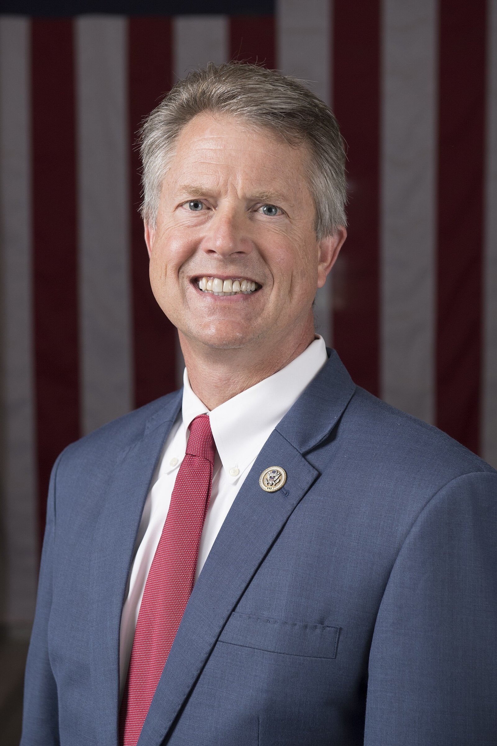 Official portrait of Roger Marshall in a blue suit and red tie, smiling in front of an American flag.