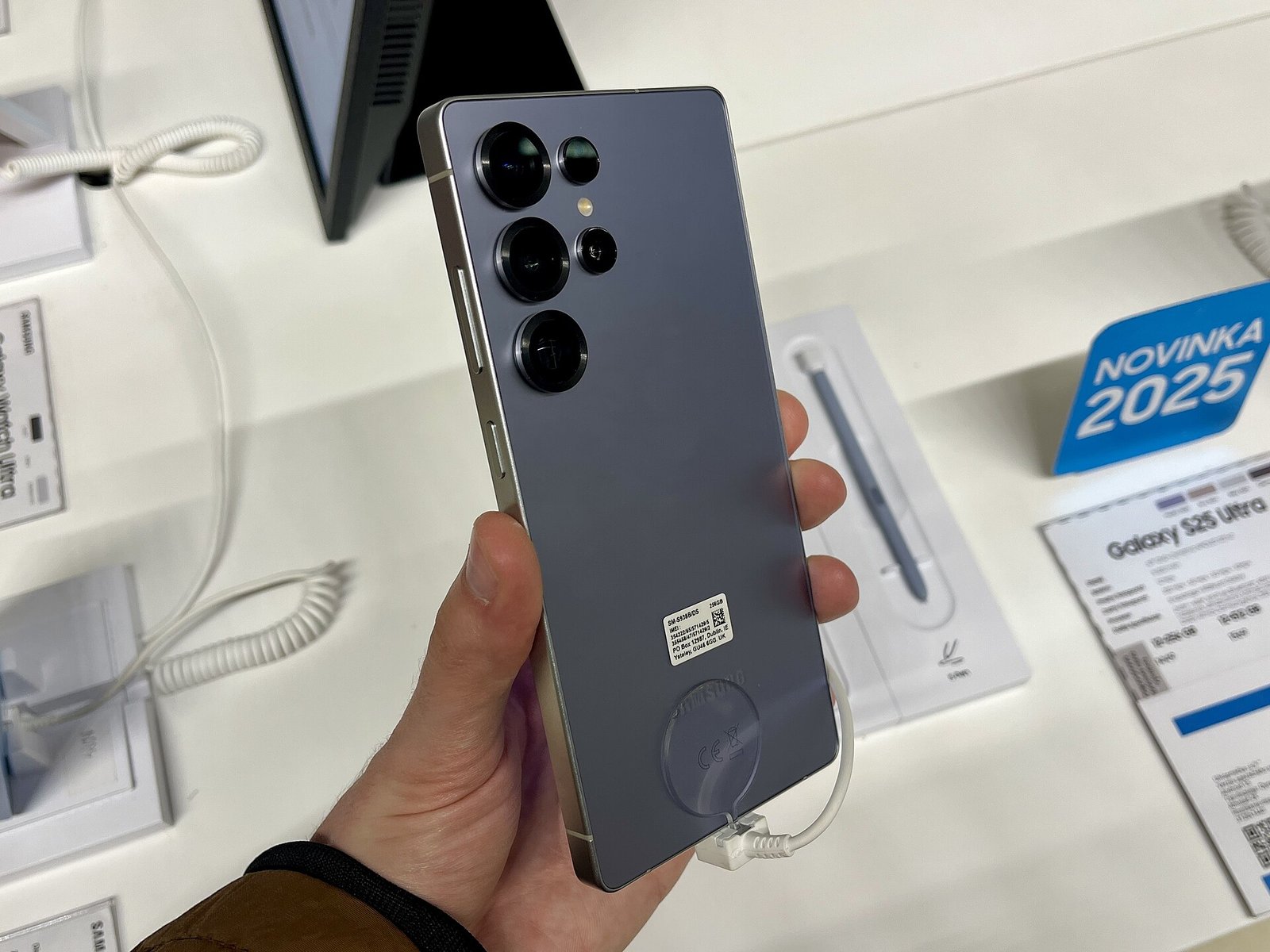 A hand holding a titanium silver-blue Samsung Galaxy S25 Ultra, showing its rear camera lenses, at a store display.