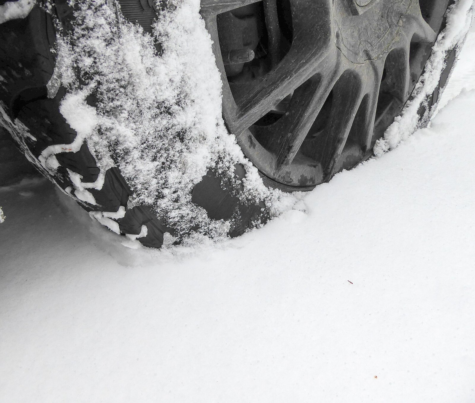 Close-up of a car's winter tire and wheel rolling through fresh powdery snow.