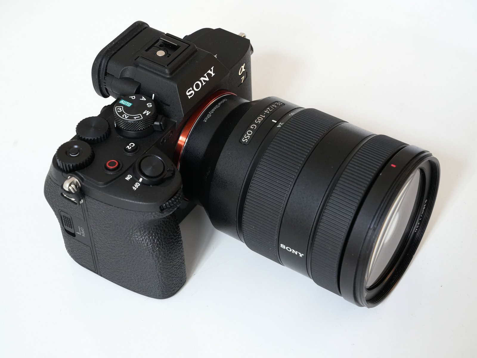 A black Sony Alpha 7 IV mirrorless camera body fitted with a large Sony zoom lens, photographed on a white background.
