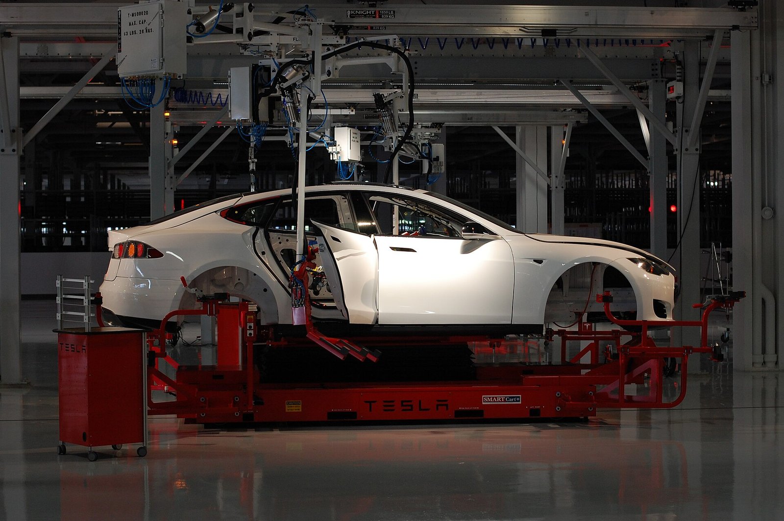 A white Tesla car body suspended on red robotic assembly equipment inside the Tesla factory in Fremont, California.