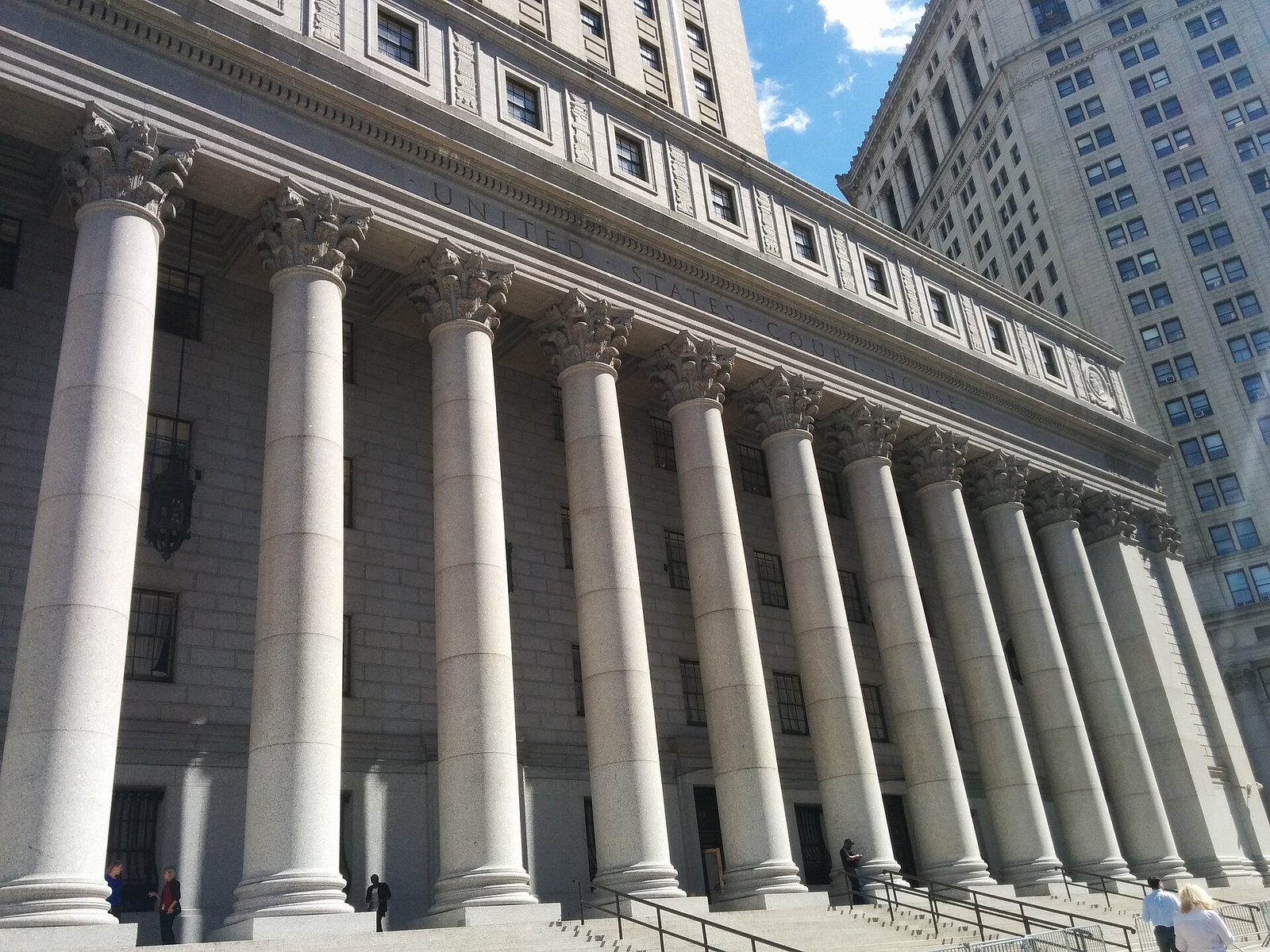 Tall stone Corinthian columns on the facade of the Thurgood Marshall United States Courthouse in New York, seen from below.