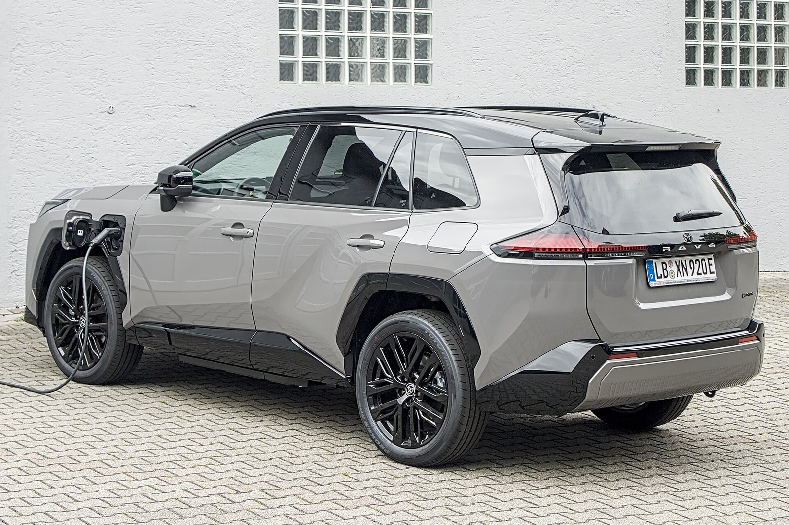 A silver new-generation Toyota RAV4 plug-in hybrid SUV parked with a charging cable plugged into its rear side.