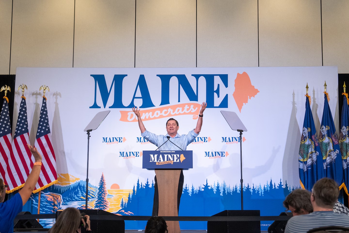 Troy Jackson raises his arms on stage at the Maine Democrats convention in Bangor.