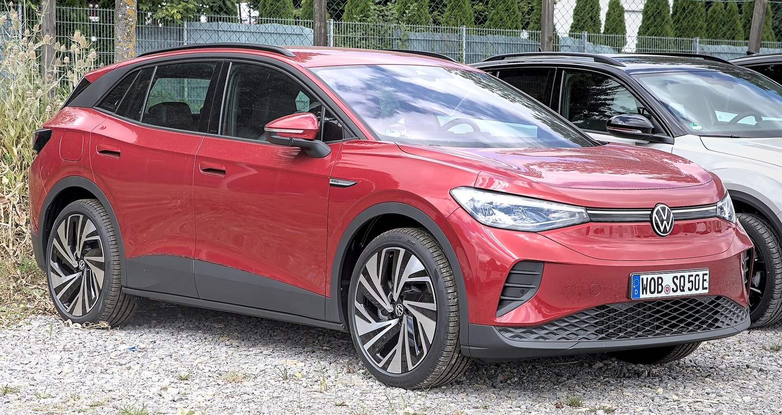 A red Volkswagen ID.4 electric compact SUV parked on gravel, seen from the front left.